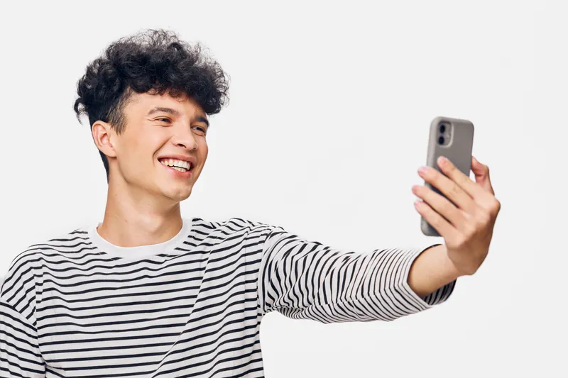 smiling man in striped shirt taking selfie with smartphone, cheerful expression, isolated on white background, casual style and youthful vibe