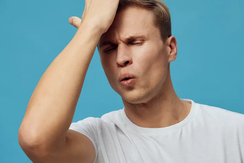 frustrated young caucasian man wear white t-shirt touch forehead with closed eyes isolated on grey background mental health concept