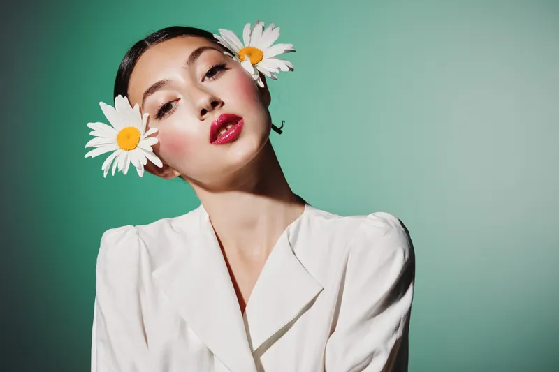 Young woman posing withean white daisies indark hair wearsplush white silk blouse againsagradaest mint background artistic beauty fashion concept.