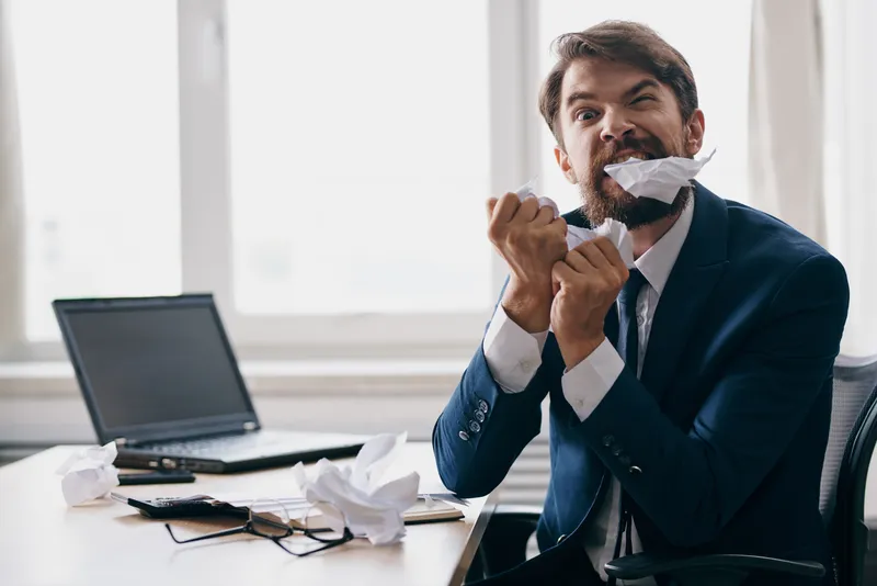 Менеджер работает за ноутбуком в офисе, на его лице эмоции недовольства, официальная обстановка