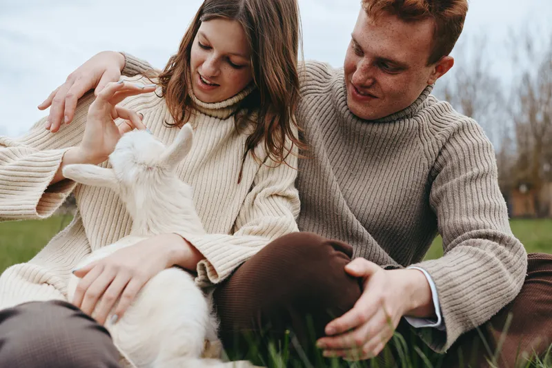 A couple outdoors with a playful goat kid, gentle touch and smiles, capturing a warm family moment in a rural setting, showcasing bonding and carefree lifestyle and nature.