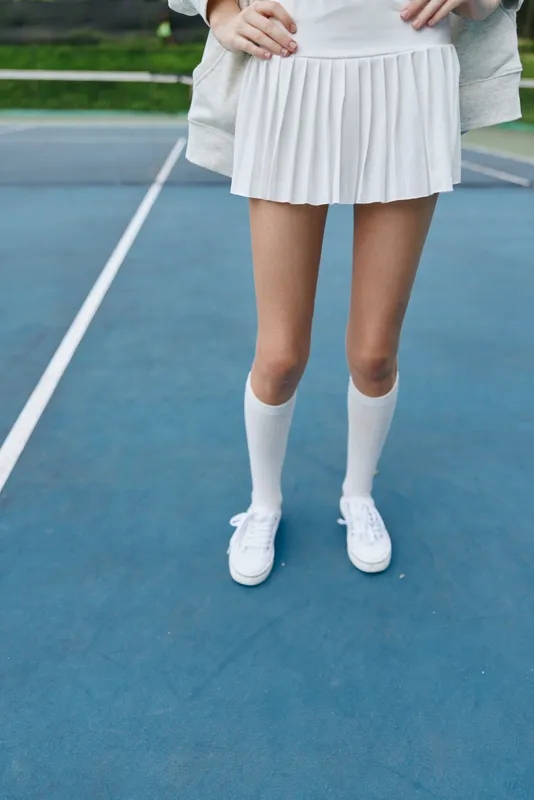 Elegant female model in a white tennis outfit, showing off her legs on a blue court, embodying a sporty and energetic vibe, perfect for summer sports themes