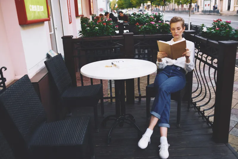 Женщина читает книгу за столиком в кафе