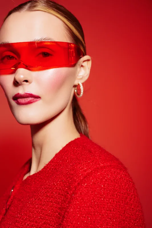 Stylish woman with red sunglasses and red outfit poses against red background. Fashion portrait with modern accessories and confident expression in studio lighting.