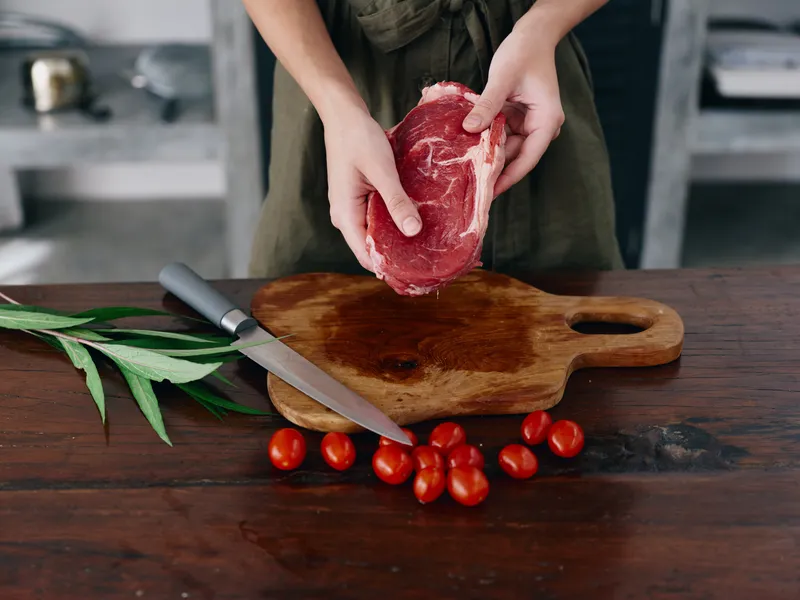 Женщина с ножом в руке нарезает свежее мясо для стейка, которое будет запекаться на кухне