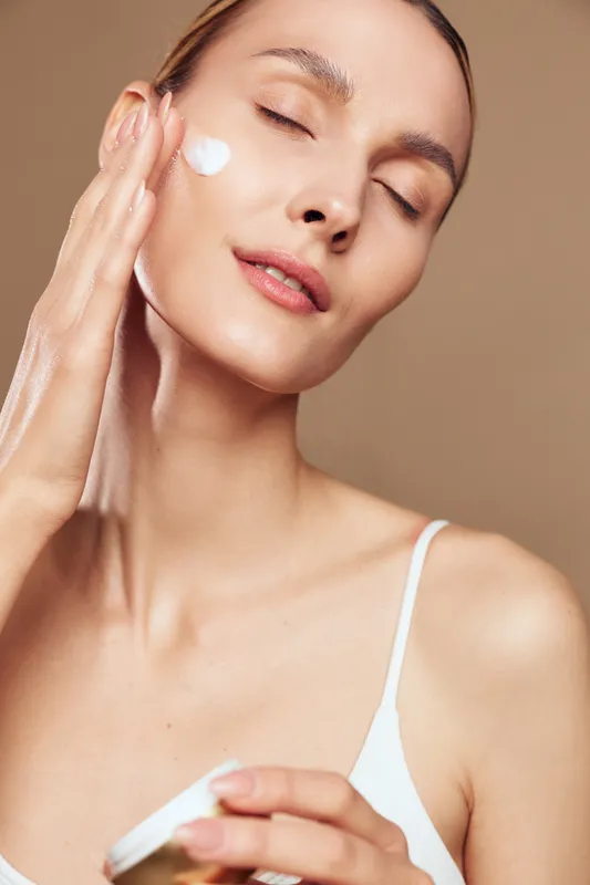 Close up of a woman applying skincare cream on her face, eyes closed, serene spa mood, bright highlights show hydration and gentle beauty treatment concept
