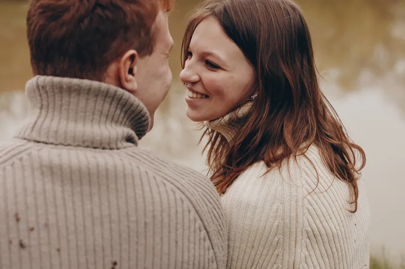Tender moment between a couple in knit sweaters outdoors, close up on their smiling faces, cozy autumn ambiance, soft light, warm tones, connection, affection, candid lifestyle