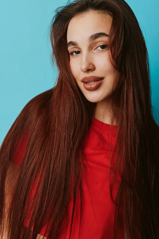 Young woman with long brown hair wearing red shirt posing and smiling on blue background, beauty portrait with natural makeup and casual style for lifestyle and fashion.
