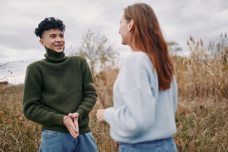 Two young adults converse in a grassy field, a natural candid scene capturing authentic interaction and credible emotions, relaxed posture and genuine connection outdoors.