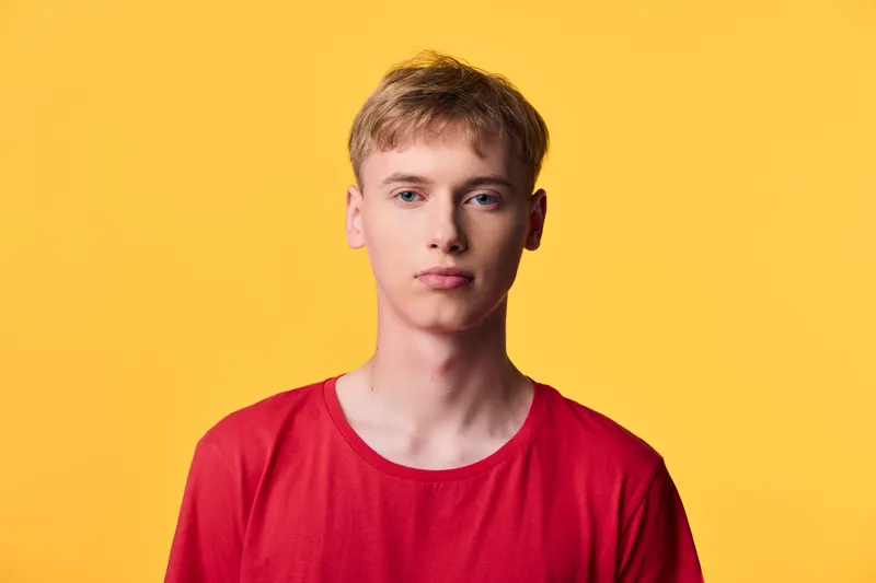 Young man in a red shirt against a bold yellow background, blond hair and a neutral expression, casual style with studio lighting for fashion, lifestyle or product showcase, bright mood and clean