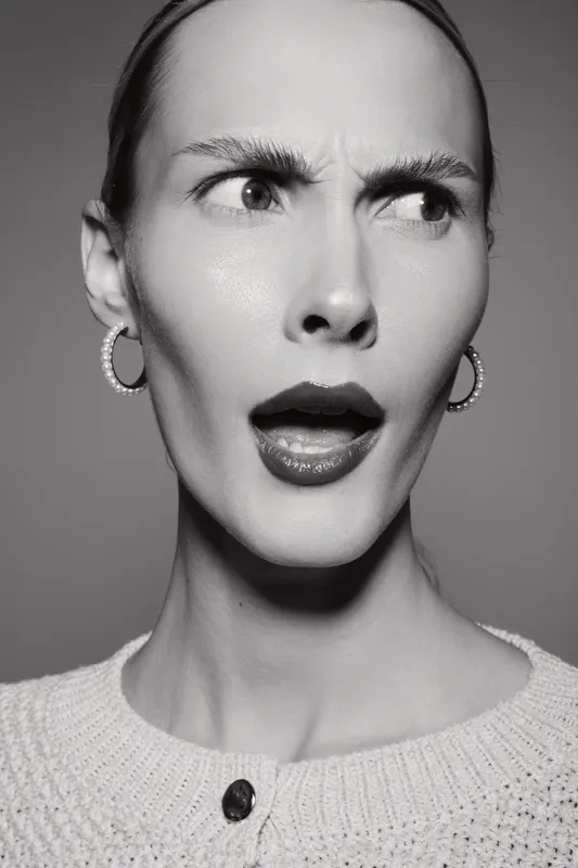 Portrait of surprised Caucasian woman with fair skin and short hair wearing earrings and sweater in black and white studio photo.