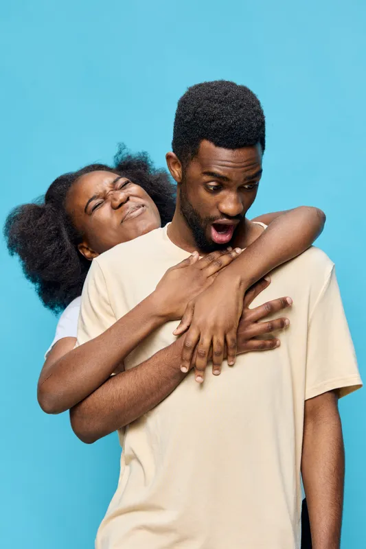 Happy couple embracing with joyful expressions against a blue background, representing love and connection in a playful and vibrant setting