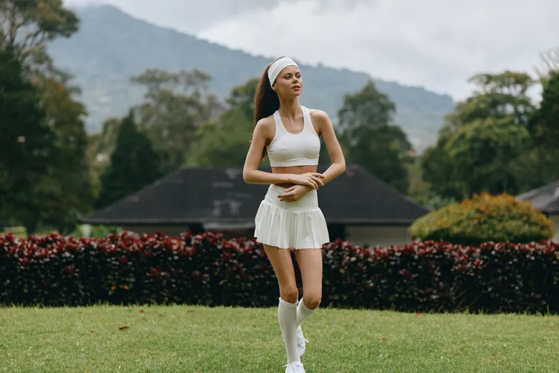Young athletic woman in white sportswear running outdoors in a serene garden setting, expressing joy and fitness, perfect for promoting a healthy lifestyle