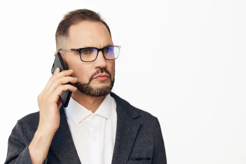 A professional businessman on a colored isolated background, speaking on a mobile phone with a focused, confident expression, conveying clear communication and decisive business mindset.