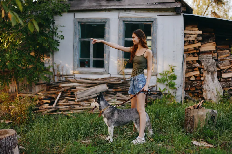 Женщина и её хаски весело играют на улице в парке среди деревьев, улыбаются, показывая зубы, во время осенней прогулки со своим питомцем