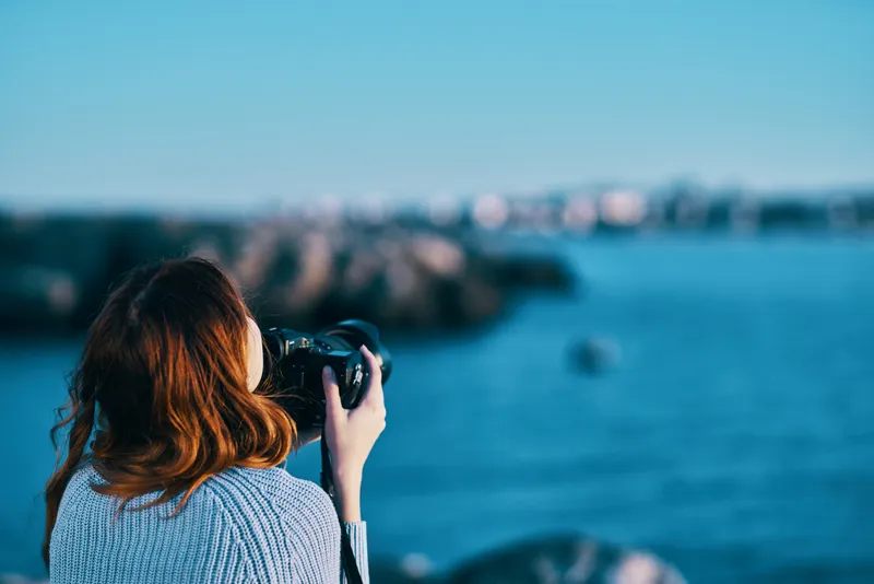 Женщина фотографирует море в горах, вид со спины