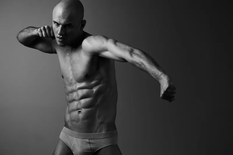 Strong man in black and white striking a punch, showcasing muscular physique with intense focus and determination, embodying strength and power.