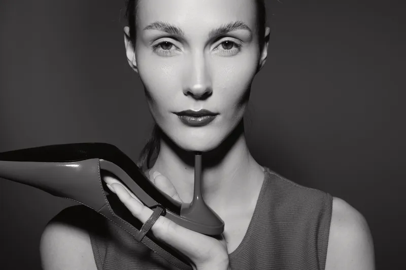 Portrait of a fair skinned white woman holding a high heel shoe near her face in black and white studio lighting. Concept of fashion, elegance, and style.