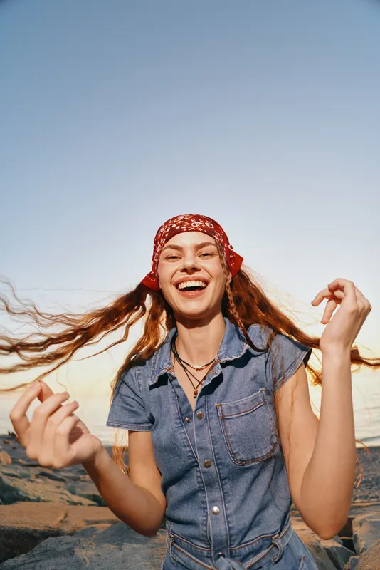 smiling woman with red bandana enjoying sunny outdoor day by water with casual denim shirt and relaxed natural background atmosphere