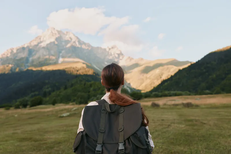 Hiker with backpack watches distant mountains, a quiet moment of reflection in wide open countryside at golden hour
