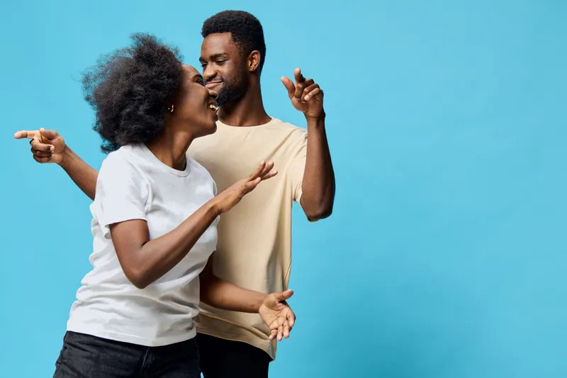 A joyful couple dancing together in front of a bright blue background, showcasing happiness and connection in a lighthearted moment
