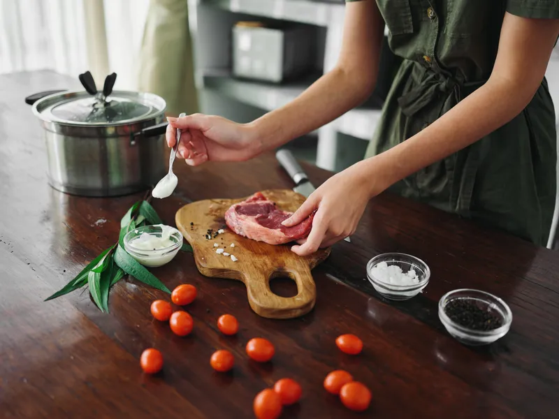 Женщина на кухне готовит ужин из мяса, овощей и специй на деревянном столе на фоне стильной кухни, крупный план рук, образ жизни