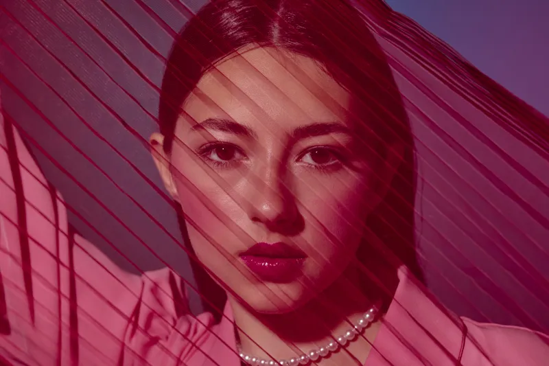 Close-up portrait of a stylish woman with bold red lipstick partially obscured by red fabric stripes. Fashion editorial concept focused on beauty, creativity, and elegance.