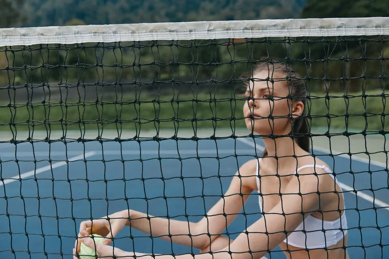 Young female tennis player preparing to serve on a sunny court, focused and determined, showcasing athleticism and the spirit of competition