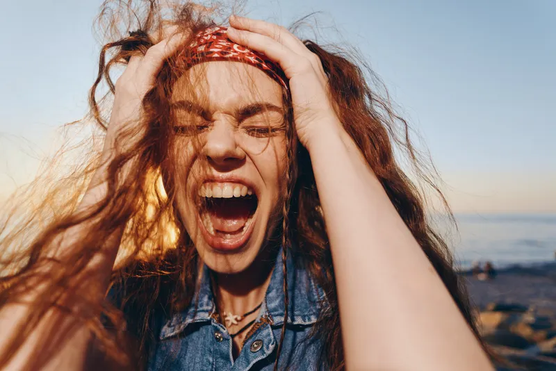 Lifestyle woman in modern boho-western denim street style screaming with passion outdoors during golden hour film color mood.