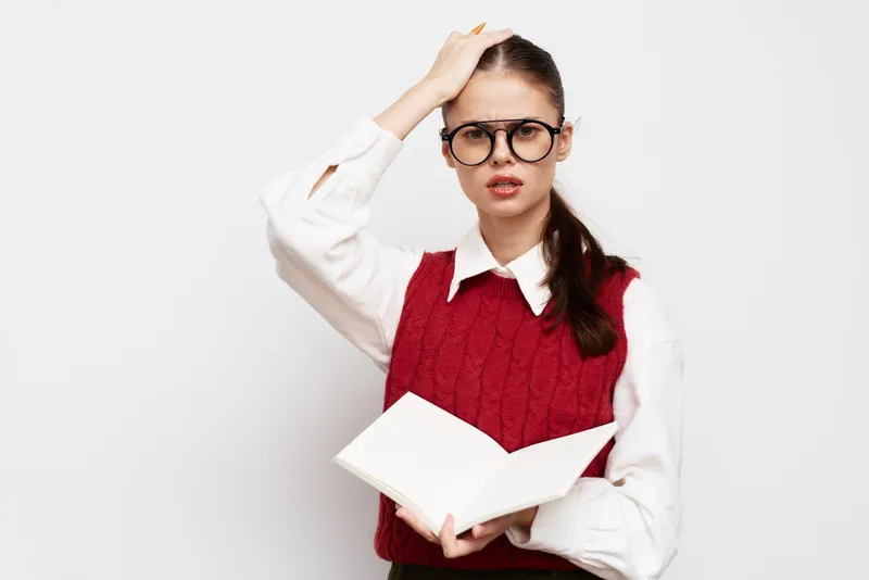 Озабоченный студент в очках держит открытую книгу, выглядит озадаченным на фоне однотонного белого фона