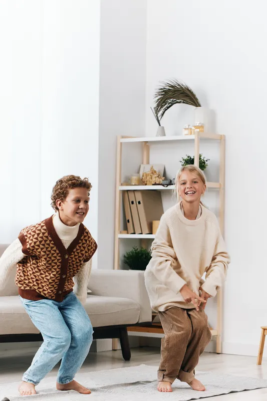 Two children playfully jump in a bright living room, capturing candid motion and joyful energy. Soft natural light, cozy furnishings, and a calm, welcoming home vibe.