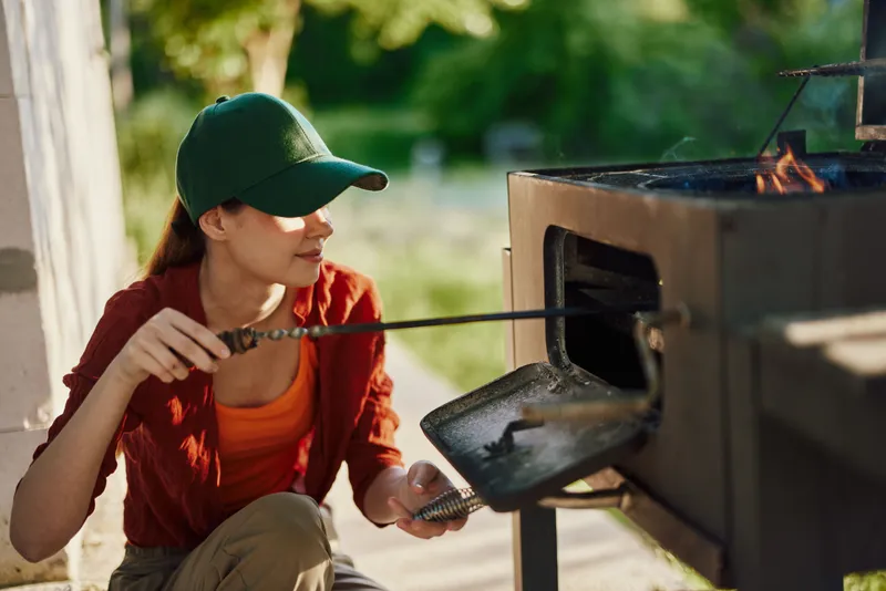 Young woman grilling fish outdoors in a sunny garden, showcasing healthy cooking, vibrant colors, and joyful emotions during a summer barbecue
