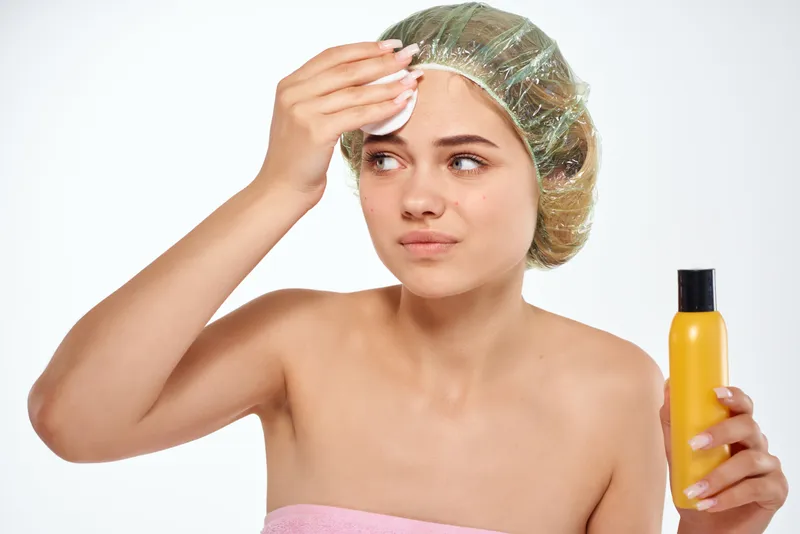 Женщина в розовом полотенце наносит лосьон на лицо