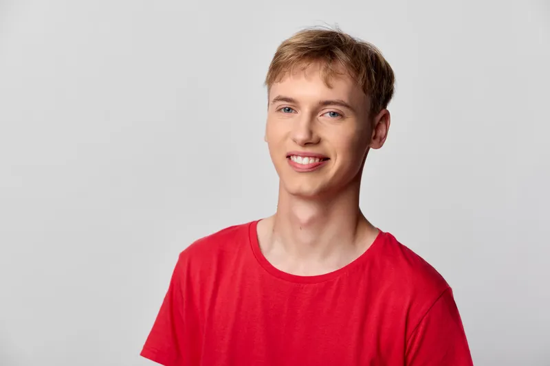 Young man wearing a red shirt with a bright smile stands in a neutral studio, casual style and clear lighting conveying friendly happiness and approachable charisma for lifestyle or ecommerce imagery