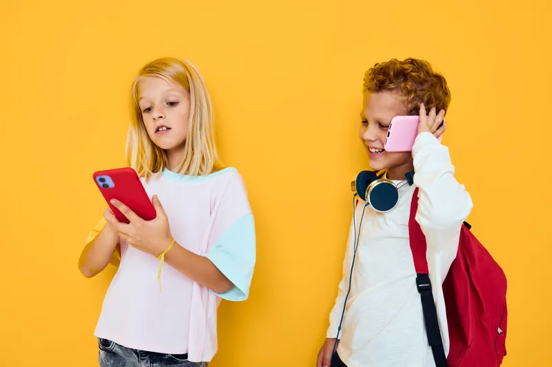 Двое детей, мальчик и девочка, используют гаджеты в наушниках