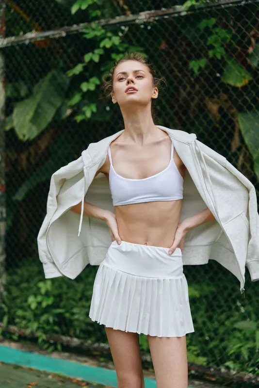 Young athletic woman in white sportswear with a confident expression, showcasing a healthy lifestyle in a serene outdoor setting Ideal for fitness and wellness themes