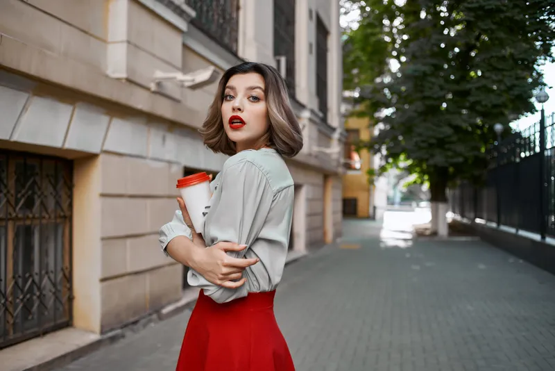 Женщина на открытом воздухе позирует для селфи с чашкой кофе, передавая атмосферу повседневной жизни