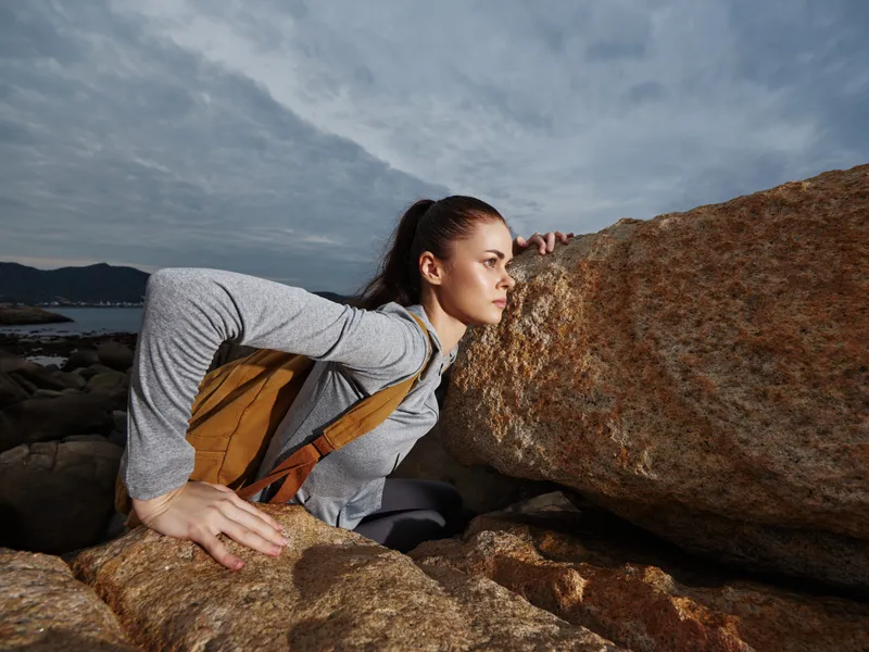 Young athletic woman exploring rocky coastline during cloudy weather, showcasing strength and determination in outdoor adventure