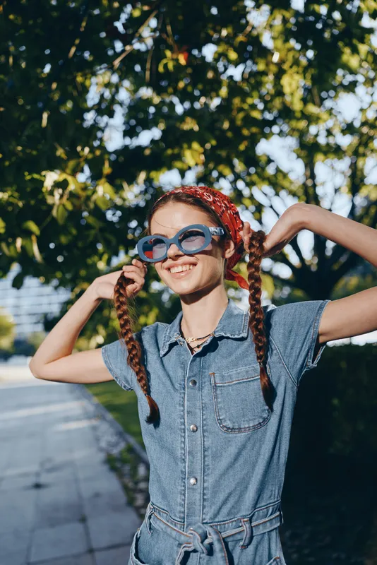 lifestyle woman in modern boho-western denim street style with red braided hair and oversized sunglasses enjoying sunny outdoors in film color aesthetic