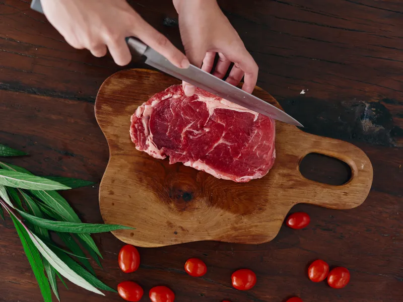 Женщина с ножом в руке нарезает свежее мясо для жарки на кухне