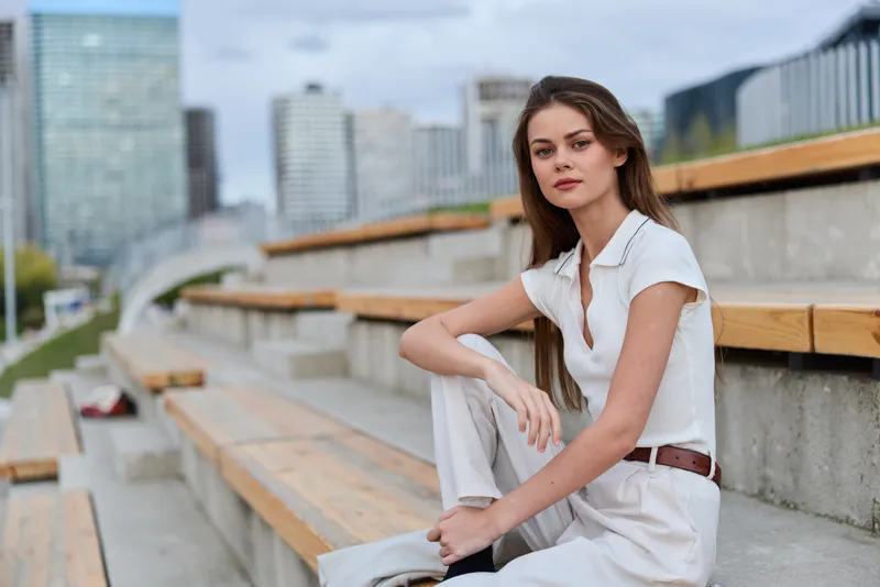 Confident businesswoman seated outdoors in a stylish light outfit, exuding professionalism and poise against a modern urban backdrop.
