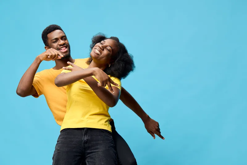 Happy young African couple enjoying playful moments together against a bright blue background, wearing casual yellow t shirts, expressing joy and positivity