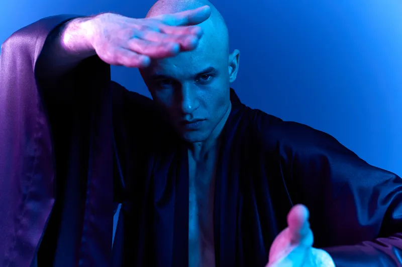 Intense man posing dramatically in a stylish black robe with a striking blue and purple light, conveying a sense of strength and determination.