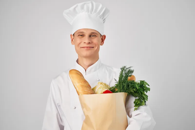 Весёлый шеф-повар мужского пола работает на кухне с упаковкой продуктов