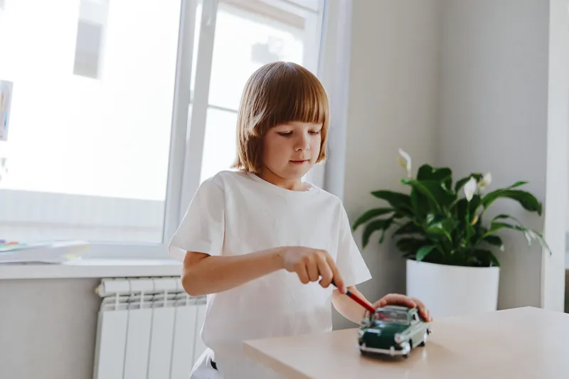 Young boy playing with a toy car, focused and engaged, bright room with natural light and green indoor plants, inspiring creativity and imagination.