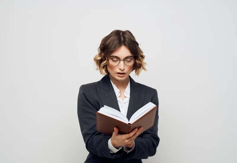 Женщина в классическом костюме с раскрытой книгой, в очках на лице, крупный план