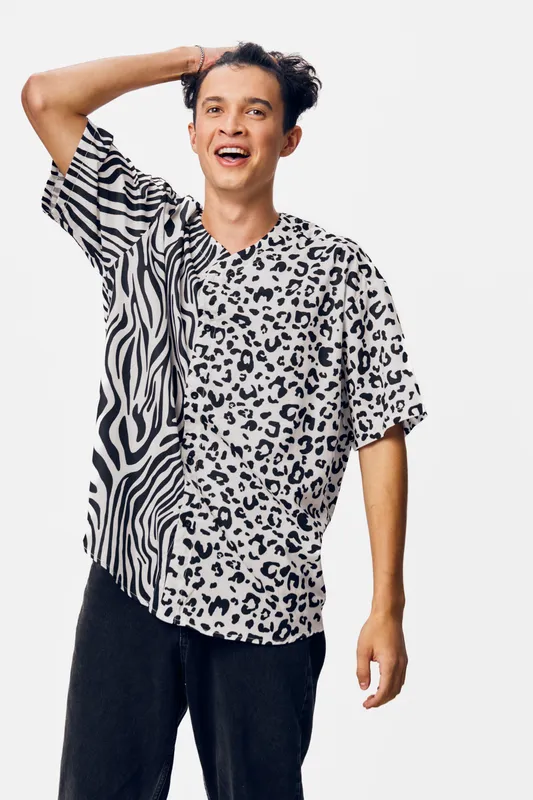 young man wearing a black and white animal print shirt, smiling cheerfully against a plain white background, casual style and joyful expression