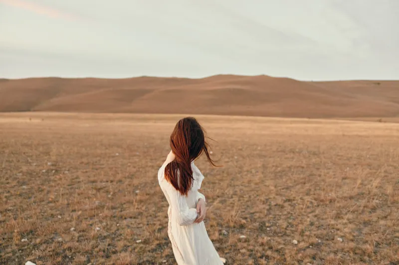Безмятежная женщина в белом платье стоит в открытом поле на закате