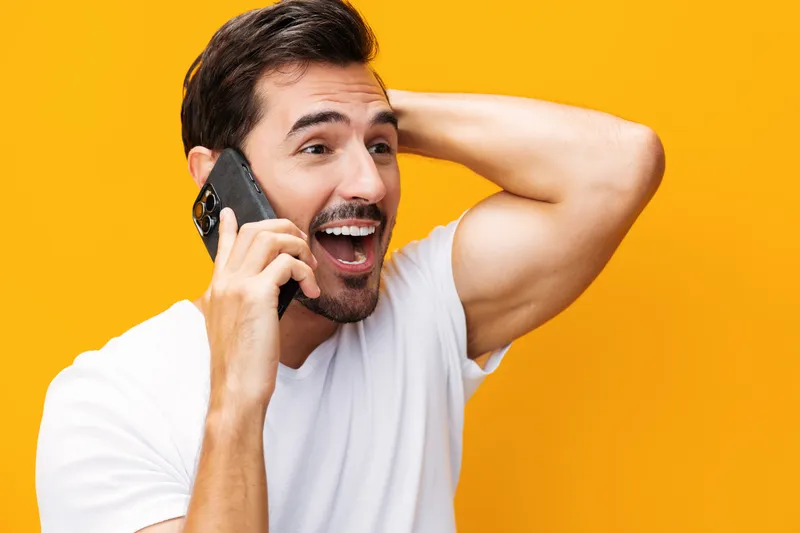 Мужчина улыбается, показывая зубы, и держит смартфон