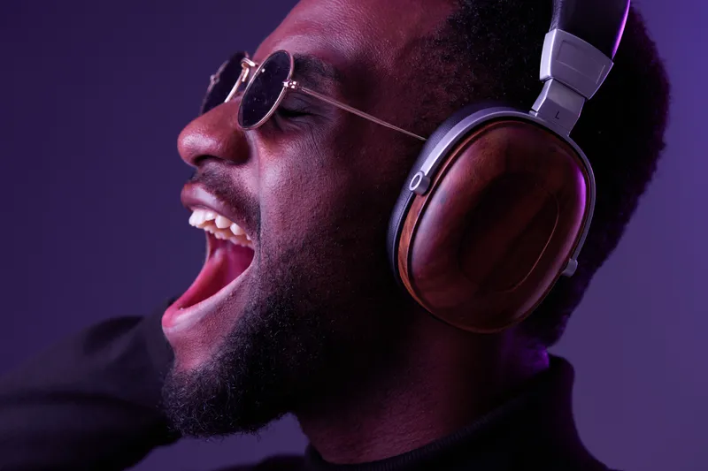 Young African man enjoying music with headphones, expressing joy and passion Dark background with purple highlights Vibrant emotions in a modern, stylish setting